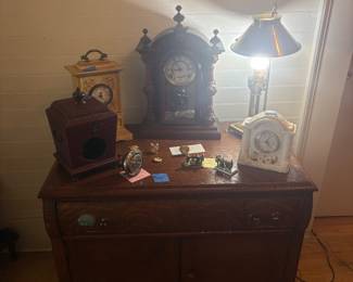 Vintage Wooden Buffet / Sideboard Cabinet Beautiful vintage wooden buffet featuring two upper drawers, double cabinet doors, decorative wood grain, and classic hardware. A charming piece perfect for a dining room, entryway, or additional storage. Also pictured are assorted vintage mantel clocks, miniature collectible clocks, and a brass table lamp. $150 buffet