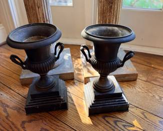Suggested Inventory Description Pair of Neoclassical-Style Black Metal Decorative Urns — Matching classical campana-form urns featuring flared rims, decorative ribbed bodies, scrolling side handles, and stepped square pedestal bases. Dark patinated finish. French Empire-inspired design.