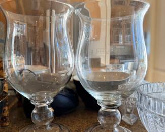 Pair of Large Clear Glass Pedestal Hurricane Vases — Matching elegant glass hurricanes featuring wide flared rims, rounded bowls, decorative baluster stems, and circular pedestal bases. Ideal for pillar candles, floral displays, or table centerpieces.