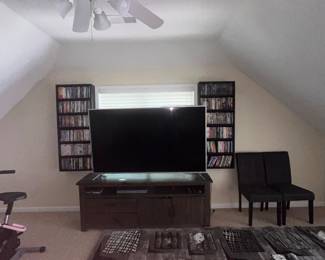 Entertainment furniture. Large TV. DVD collection, black and gray area rug. shelving units. black dining chairs.