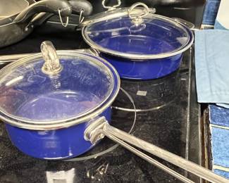 Cobalt blue enamel cookware including a saucepan and a skillet, both featuring clear glass lids and stainless steel loop handles.