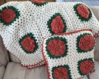 Handmade crocheted rose-motif afghan throw blanket and matching accent pillow in cream, green, and terracotta red tones.
