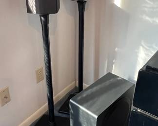 Pair of black satellite speakers on tall stands accompanied by a matching powered subwoofer.