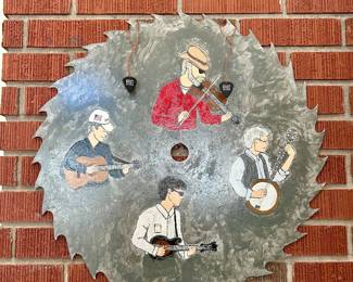 Hand-painted circular saw blade wall art featuring four bluegrass musicians with fiddle, banjo, guitar, and mandolin