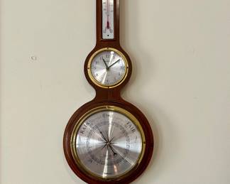 Traditional wooden wall-mounted weather station featuring a barometer, thermometer, clock, and hygrometer with brass-tone accents