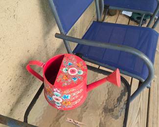 Red hand-painted floral metal watering can on blue sling chair