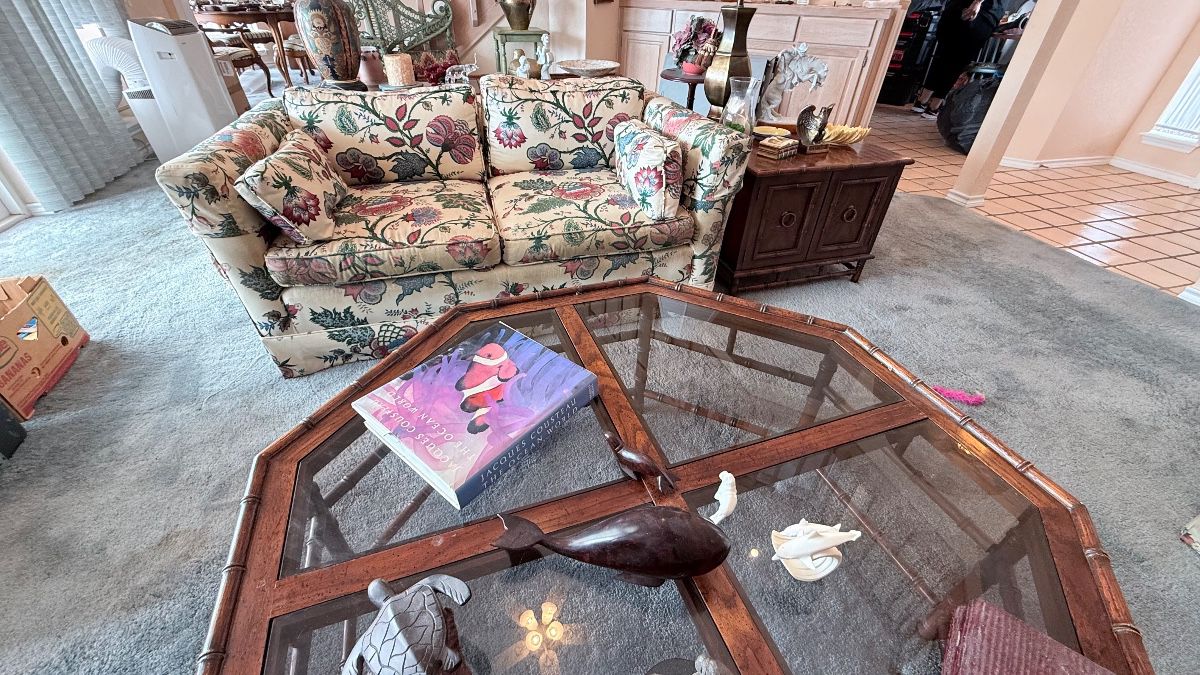Living Room Furniture & Décor Collection – Floral upholstered loveseat featuring rolled arms and matching cushions, octagonal glass-top coffee table with a wood frame, and a traditional wooden two-door end table. A charming assortment of furniture and decorative accents for a living room or sitting area.