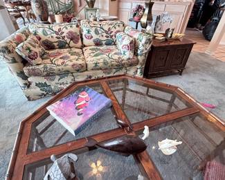 Living Room Furniture & Décor Collection – Floral upholstered loveseat featuring rolled arms and matching cushions, octagonal glass-top coffee table with a wood frame, and a traditional wooden two-door end table. A charming assortment of furniture and decorative accents for a living room or sitting area.