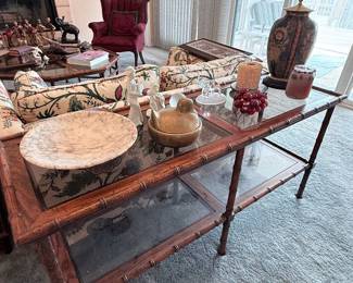 Vintage bamboo-style glass-top sofa table with lower glass shelf, featuring assorted decorative accents and collectibles.