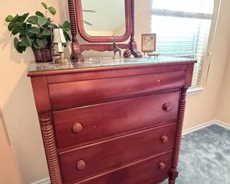 Vintage wooden three-drawer dresser with marble top, turned column detailing, and matching swivel mirror.
