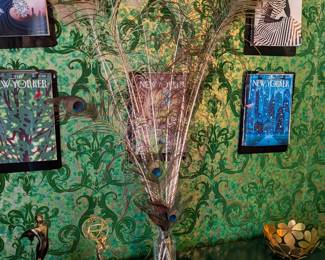 Peacock feathers in glass jar. New Yorker magazine covers with clipboards. Gold brass flower bowl.