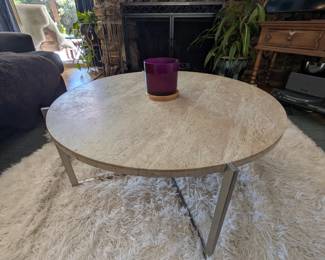 Round travertine stone coffee table with silver metal base, made in Mexico. Cream faux fur shag rug (Silhouette Home). Wrought iron fireplace tool set.