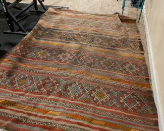 Tribal striped kilim area rug in rust, orange, gray and blue geometric patterns. Boho vintage style. Teal wire shelving rack also shown.
