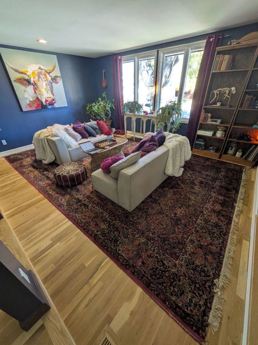 Pair of dove gray loveseats, modern sofas. Vintage-style woven wicker coffee table. Karastan wool rug, red Persian Oriental pattern. Large schefflera umbrella tree in glazed ceramic pot. Colorful velvet throw pillows. Wood serving tray, chess set.