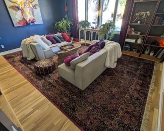 Pair of dove gray loveseats, modern sofas. Vintage-style woven wicker coffee table. Karastan wool rug, red Persian Oriental pattern. Large schefflera umbrella tree in glazed ceramic pot. Colorful velvet throw pillows. Wood serving tray, chess set.