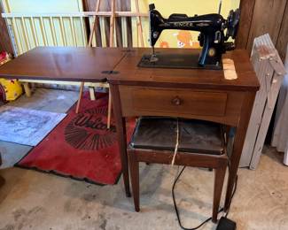 Vintage black singer sewing machine mounted inside a wooden drop-leaf desk with matching cushioned stool