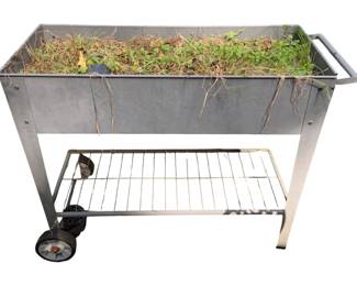 1121 - Metal Planter 32"x41"x16" (Description): Metal planter on wheels with lower wire shelf. Features side handles for easy maneuvering. Measures 32" x 41" x 16".