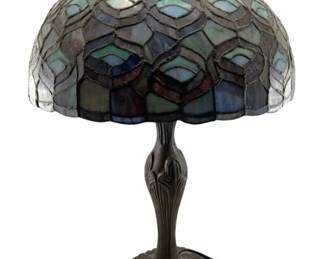 677 - Stained Glass Lamp 22" (Description): A stained glass lamp featuring a decorative shade with colorful glass panels in shades of blue, purple, green, and white arranged in an intricate peacock feather-inspired pattern. The shade sits atop a cast metal base with ornate detailing. Measures 22 inches in height. Used as-is electric/electronic/mechanical item. No guarantee all components present, untested if not otherwise stated.