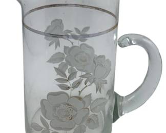 296 - Glass Pitcher 7" (Description): Glass pitcher featuring a decorative floral design with silver trim at the rim. The pitcher has a classic form with a shaped pouring spout and applied handle.