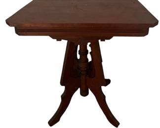 723 - Wooden Victorian Parlor Table (Description): Wooden Victorian table featuring a square top with beveled edges and a decorative pedestal base with four splayed legs. Measures 28 inches by 27 inches by 19 inches.