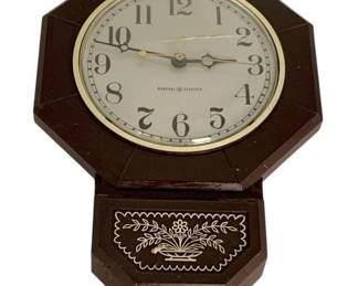 1077 - General Electric Corded Wall Clock 10"x7" (Description): General Electric corded wall clock featuring a brown octagonal case with decorative floral motif on the upper portion. The clock face displays Arabic numerals with a brass-toned bezel. Measures 10 inches by 7 inches. Used as-is electric/electronic/mechanical item. No guarantee all components present, untested if not otherwise stated.