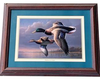 1129 - James Hautman Mallards in Flight Print (Description): A framed James Hautman print titled "Mallards in Flight," depicting a pair of mallard ducks in mid-flight against a dramatic sky. The print is double matted with teal and cream mats and set in a dark wood frame. Measures 14.5" x 18.5" overall.