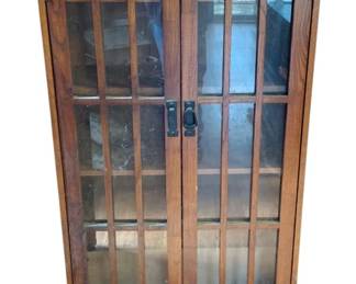 1043 - Two Door Wood Bookcase (Description): Two door wood bookcase featuring glass-paned doors with vertical mullions. One handle is broken. Measures 48 inches tall by 26 inches wide by 9 inches deep.