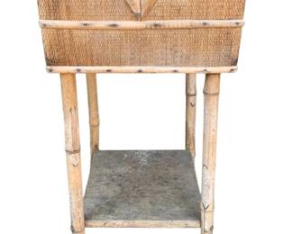 1024 - Wicker Sewing Stand 29"x14"x14" (Description): A wicker sewing stand with bamboo-style legs and a lower shelf. The piece shows damage and wear consistent with age. Measures 29 inches tall by 14 inches wide by 14 inches deep.