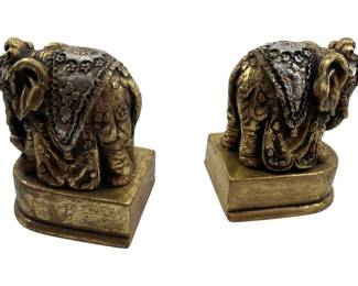 306 - Pair Elephant Bookends 5"x3"x4" (Description): Pair of decorative elephant bookends featuring ornate detailing and a gold-toned finish. Each bookend depicts an elephant in traditional ceremonial dress.