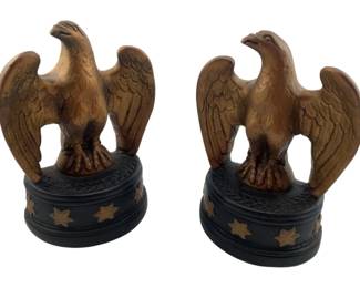307 - Pair Eagle Bookends 9"x6"x2" (Description): A pair of decorative eagle bookends. Each bookend features a spread-wing eagle figure in a golden bronze finish, perched atop a dark round base adorned with stars. Measures 9 inches by 6 inches by 2 inches.