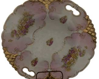 270 - Floral Porcelain Platter w/ Rack 11" (Description): A decorative porcelain platter featuring floral motifs with pink and gold accents along a scalloped edge with pierced handles. Comes with a display rack. Measures 11 inches in diameter.