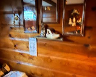 Knotty pine log-style paneled wall featuring mounted wooden shadow boxes, brass sconces, and decorative shelf figurines.