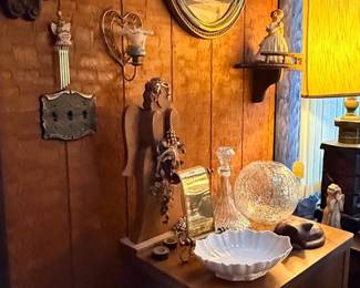 Collection of vintage home decor including wall art, heart sconces, a wooden side table, glass decanter, crackle glass globe, and a large nutcracker.