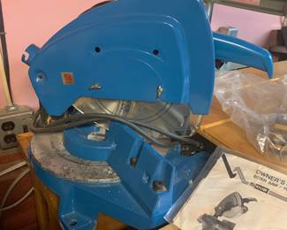 Vintage blue Ryobi TS-251U miter saw sitting on a workbench alongside its original owner's manual.