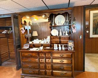 Vintage dark pine hutch dresser with attached mirror and shelving unit, decorated with decorative porcelain figurines and glassware.