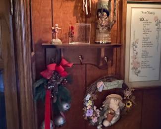 Rustic home decor display featuring a wall-mounted wooden shelf, ceramic beer stein, decorative wreaths, holiday door bells, framed artwork, and wooden goose accent.