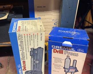 Vintage Dremel power tool attachment boxes including a Deluxe Moto-Lathe Kit Model 701, a Drill Press Model 210, and a Disc-Belt Sander Model 730 box.