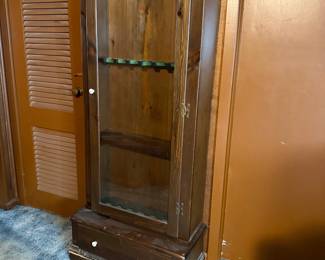 Vintage dark pine wooden gun cabinet featuring a single glass-front door, felt-lined racks, and a bottom storage drawer.