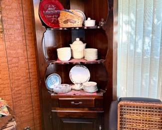 Vintage dark stained wood corner hutch cabinet with scalloped shelving frames, filled with decorative plates, bowls, and dishware.