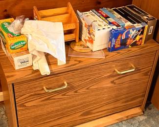 Oak-veneer low filing cabinet with brass handles, topped with various household items including VHS tapes and sandwich bags.