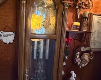 Vintage oak grandfather clock with an ornate bonnet top, brass moon phase dial, and decorative pendulum.