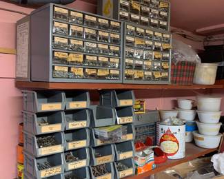 Assorted workshop hardware storage, including metal drawer organizers and stacked plastic bins filled with various screws, nails, and fasteners.