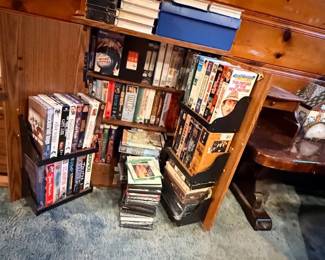 Large collection of VHS tapes and DVDs arranged in small wooden storage racks and on shelves.