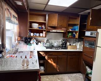 Vintage 1970s kitchen featuring dark wood cabinetry filled with glassware, kitchenware, small appliances, and a built-in wall oven.