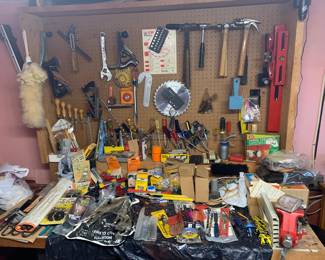 Wooden workbench and pegboard wall filled with various hand tools, hardware, clamps, and vintage shop accessories.