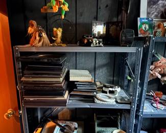 Metal shelving unit filled with eclectic collectibles, including picture frames, plush toys, maracas, framed artwork, and home decor items.