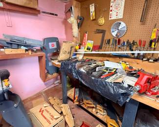 Workshop area filled with various woodworking power tools and hand tools, including a band saw, jointer, red bench vise, hand saws, and pegboard-mounted accessories.