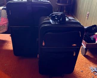 Pair of modern black fabric rolling suitcases in different sizes with zippered exterior pockets.