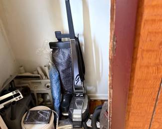 Vintage Kirby Generation 4 upright vacuum cleaner with attachments, owner's manual VHS, and caddy stored in a closet.