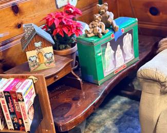 Rustic wooden coffee table with a small desk top section, holding decorative items including a house-shaped candle holder, artificial poinsettia, teddy bear figurines, and a boxed nativity set.